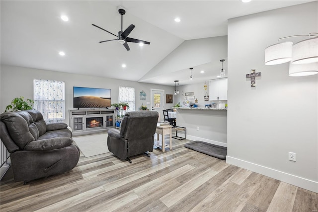 living room featuring light wood finished floors, recessed lighting, ceiling fan, a warm lit fireplace, and baseboards