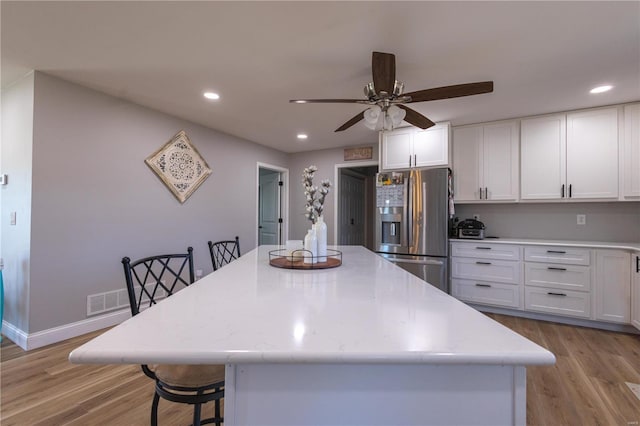 kitchen featuring light wood finished floors, recessed lighting, stainless steel fridge, and white cabinets