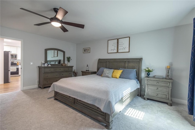 bedroom featuring a ceiling fan, freestanding refrigerator, light carpet, and baseboards