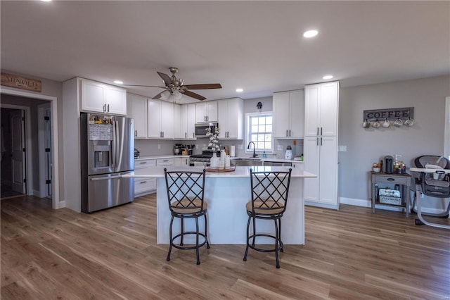 kitchen featuring stainless steel appliances, wood finished floors, a kitchen island, white cabinetry, and light countertops