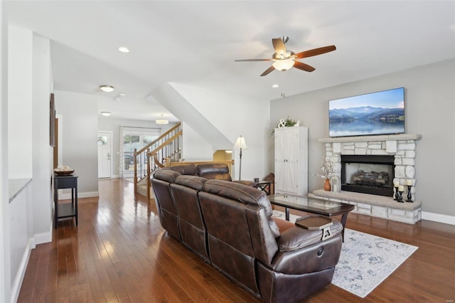 living room with baseboards, stairway, a fireplace, a ceiling fan, and dark wood-style flooring