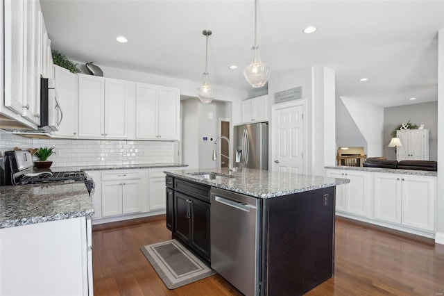 kitchen with a kitchen island with sink, a sink, light stone counters, appliances with stainless steel finishes, and dark wood-style flooring