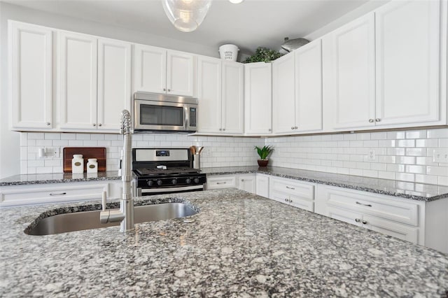 kitchen featuring dark stone countertops, backsplash, appliances with stainless steel finishes, and white cabinets