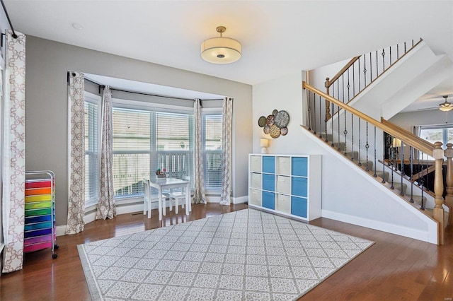 interior space with a ceiling fan, stairs, baseboards, and wood finished floors