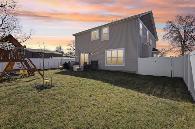 rear view of house with a lawn, a playground, a fenced backyard, and a gate