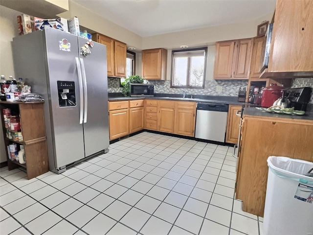 kitchen featuring stainless steel appliances, dark countertops, backsplash, light tile patterned flooring, and a sink