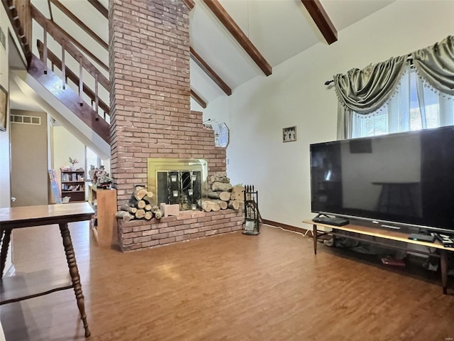 living area with beam ceiling, visible vents, a brick fireplace, wood finished floors, and high vaulted ceiling