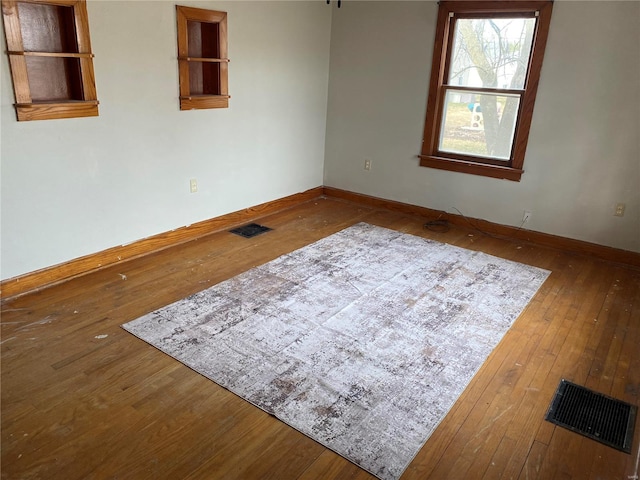 empty room featuring wood-type flooring, visible vents, and baseboards