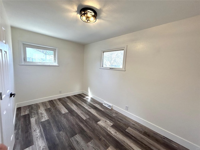 empty room featuring a wealth of natural light, dark wood-style flooring, visible vents, and baseboards