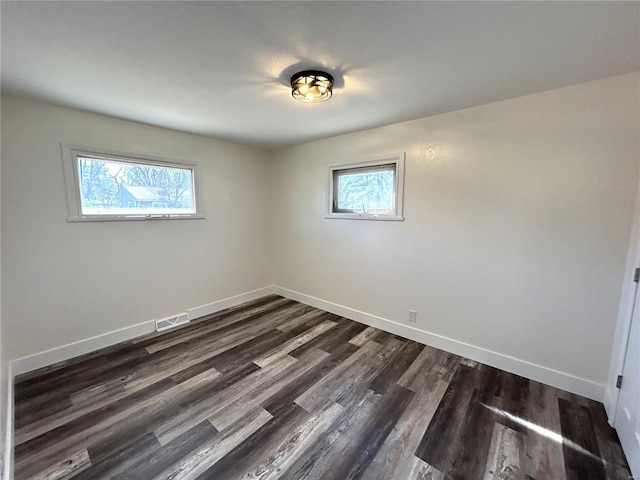 spare room featuring baseboards, dark wood-type flooring, visible vents, and a healthy amount of sunlight