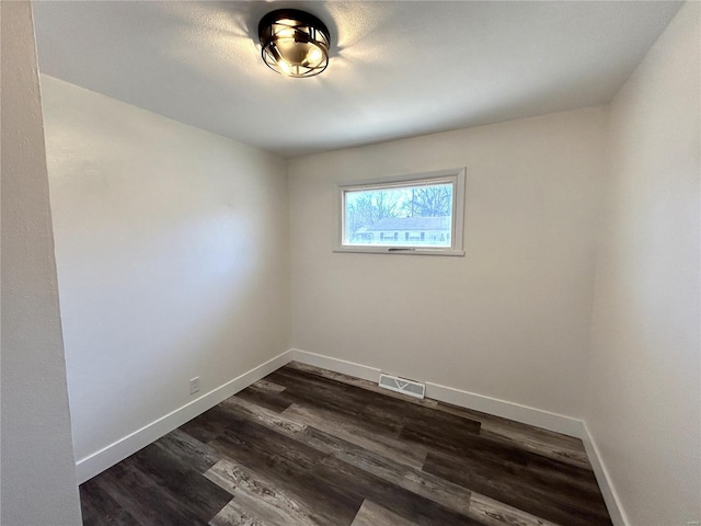 empty room with dark wood-style floors, visible vents, and baseboards