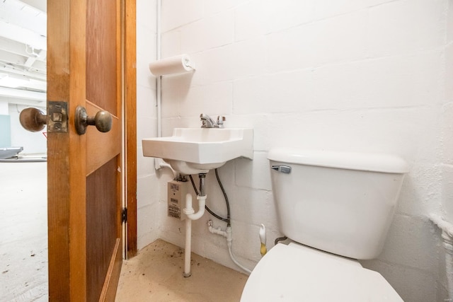 half bathroom featuring unfinished concrete floors, toilet, concrete block wall, and a sink