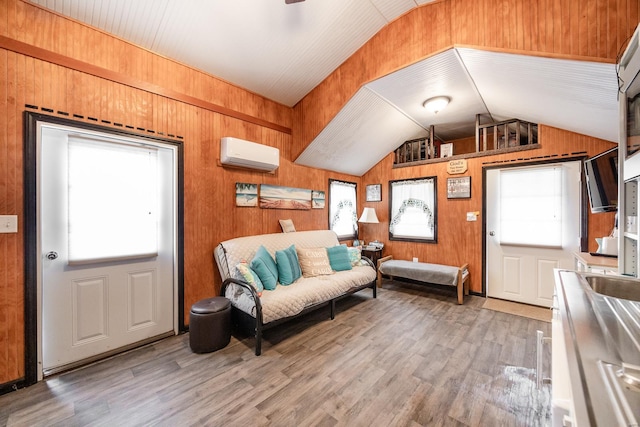 living room featuring vaulted ceiling, light wood-style floors, wood walls, and a wall mounted air conditioner