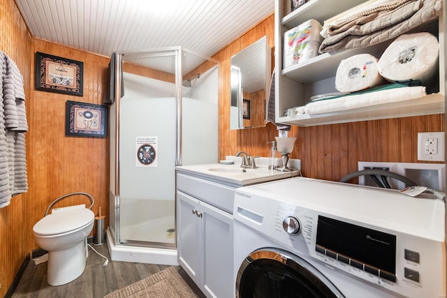 clothes washing area featuring wooden walls, wood finished floors, washer / dryer, laundry area, and a sink