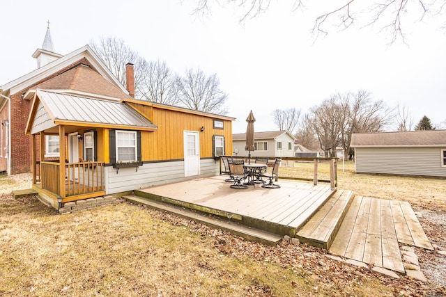 back of house with a chimney, a wooden deck, outdoor dining area, and brick siding