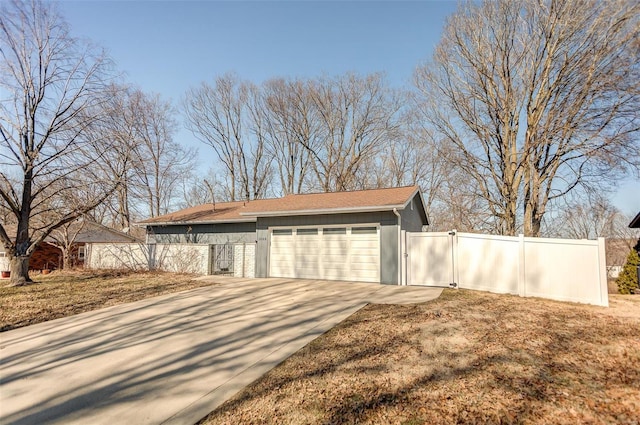 garage featuring concrete driveway, fence, and a gate