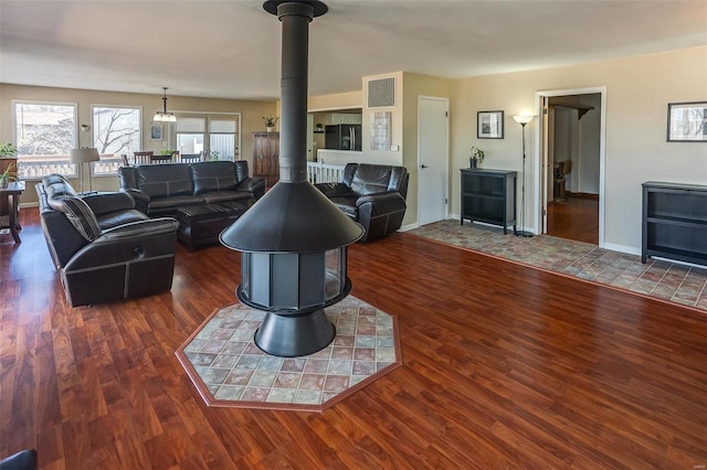 living area featuring a wood stove, visible vents, baseboards, and wood finished floors