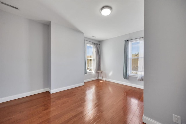 empty room with visible vents, baseboards, and hardwood / wood-style flooring