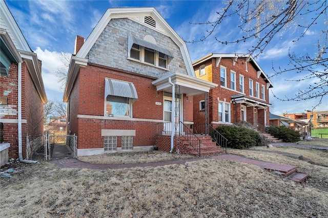 view of front of house featuring brick siding, a gate, and a gambrel roof