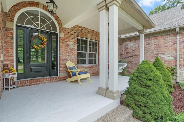 entrance to property with a porch, a shingled roof, and brick siding