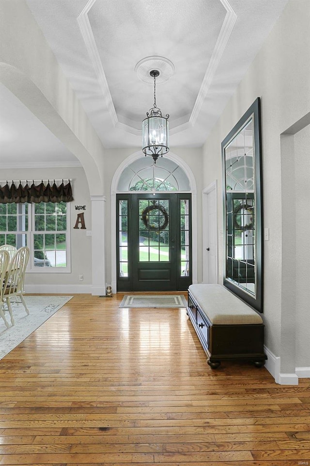 foyer entrance with a chandelier, hardwood / wood-style flooring, baseboards, ornamental molding, and a raised ceiling