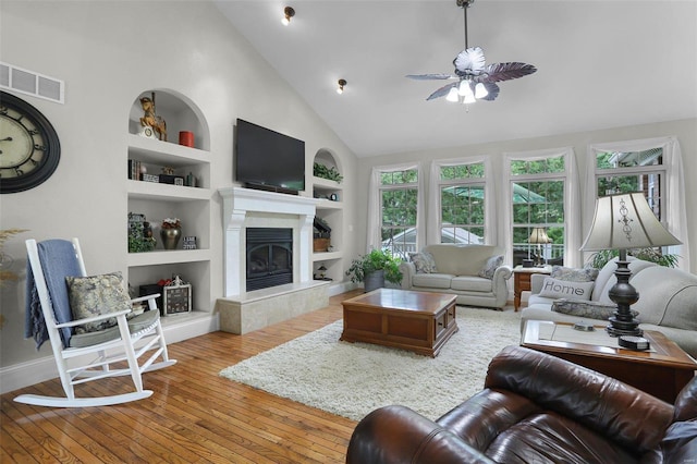 living area featuring high vaulted ceiling, hardwood / wood-style flooring, visible vents, built in features, and a glass covered fireplace