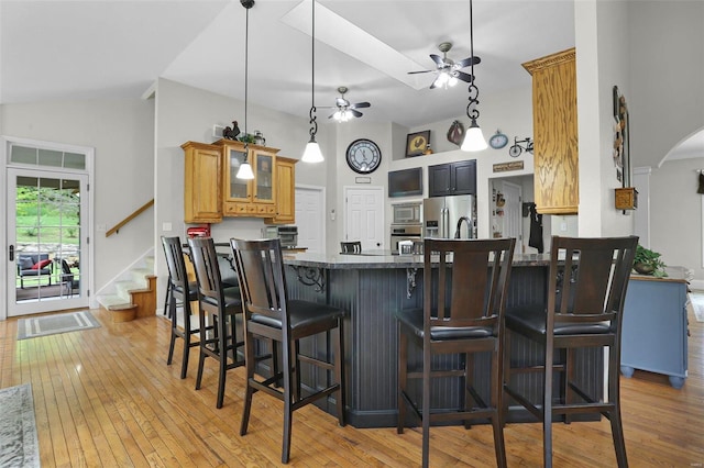 kitchen featuring arched walkways, light wood-style flooring, glass insert cabinets, stainless steel appliances, and a kitchen bar