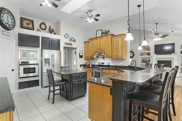 kitchen featuring a breakfast bar area, appliances with stainless steel finishes, a sink, ceiling fan, and under cabinet range hood