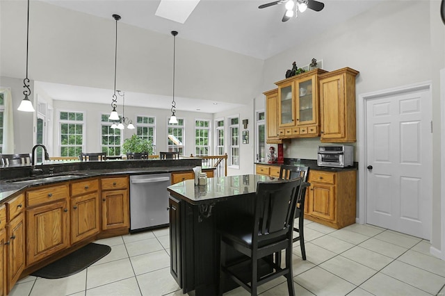 kitchen with light tile patterned floors, stainless steel dishwasher, brown cabinetry, a sink, and vaulted ceiling with skylight