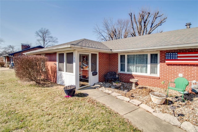 single story home with a shingled roof, brick siding, a chimney, and a front lawn