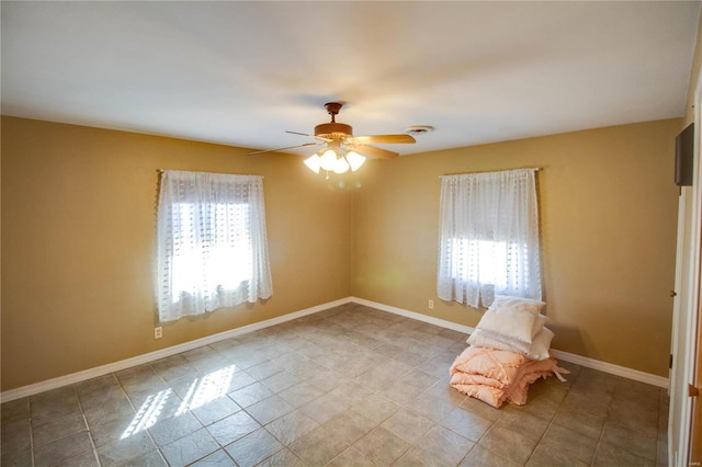 spare room featuring a ceiling fan, plenty of natural light, and baseboards