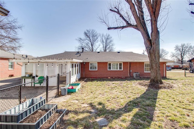 back of house featuring a garden, fence, a yard, central air condition unit, and brick siding