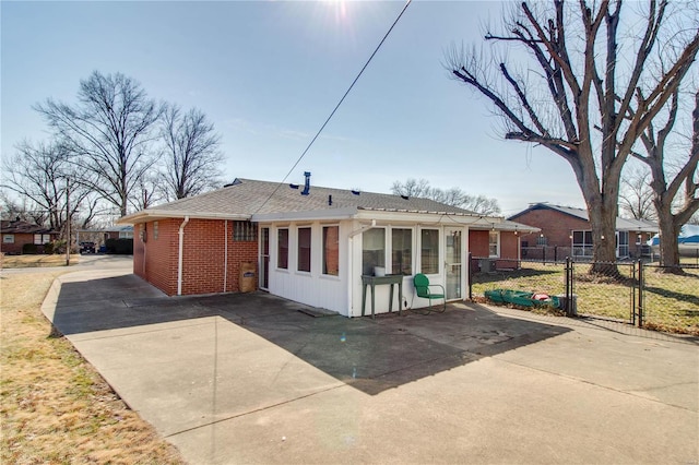 view of front of home with brick siding, fence, a patio, and roof with shingles