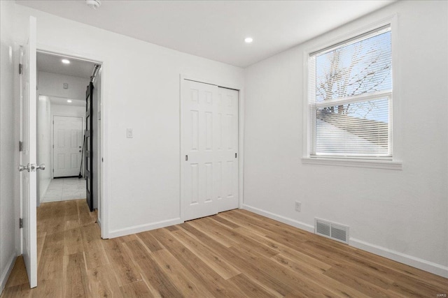 unfurnished bedroom featuring light wood finished floors, baseboards, visible vents, and a closet