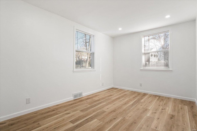 empty room featuring light wood-type flooring, a wealth of natural light, visible vents, and baseboards