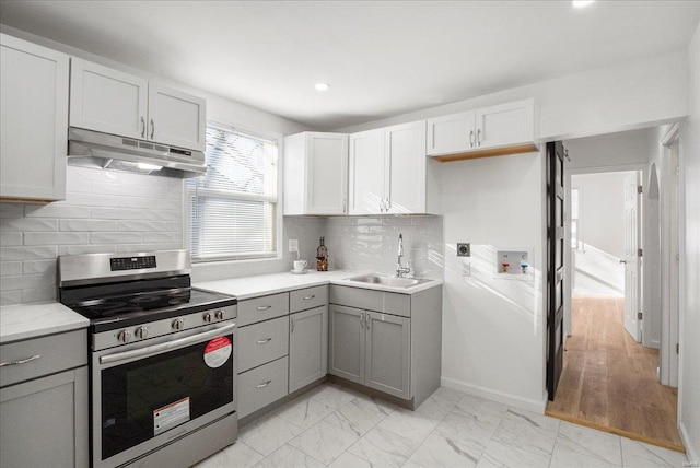 kitchen with gray cabinets, stainless steel electric range oven, under cabinet range hood, and a sink