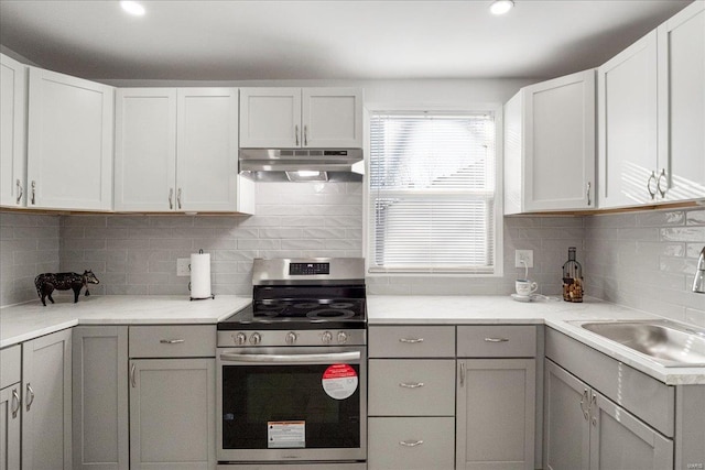 kitchen featuring under cabinet range hood, a sink, gray cabinets, tasteful backsplash, and stainless steel range with electric stovetop