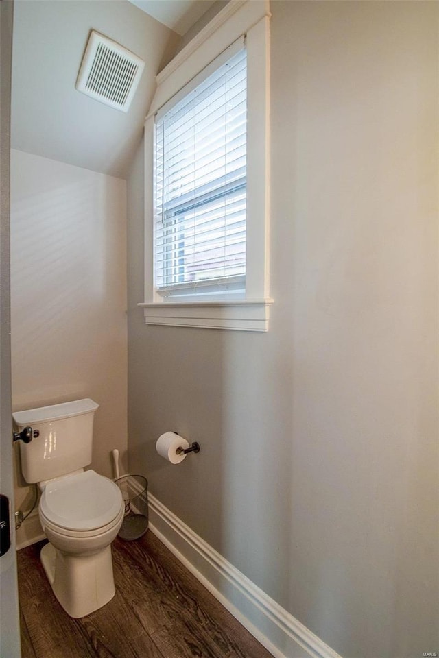 half bathroom with baseboards, visible vents, toilet, lofted ceiling, and wood finished floors