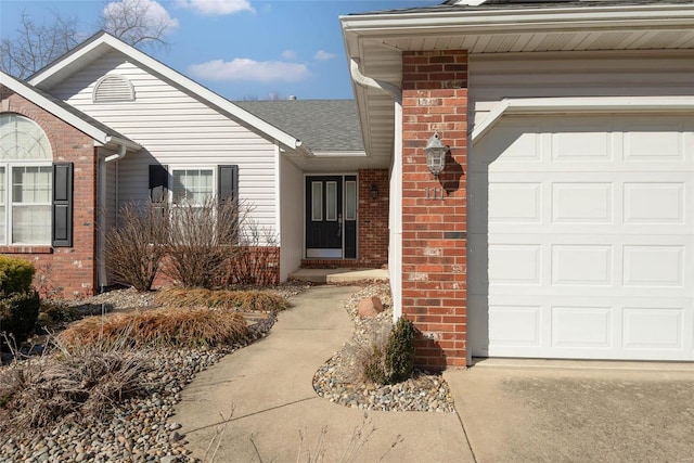 view of exterior entry featuring a garage, brick siding, and a shingled roof