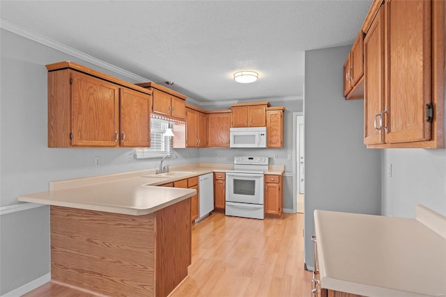 kitchen with a peninsula, white appliances, a sink, light wood-type flooring, and crown molding