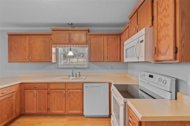 kitchen with brown cabinetry, white appliances, a sink, and ornamental molding