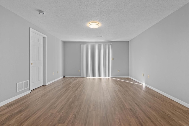 empty room with baseboards, a textured ceiling, visible vents, and wood finished floors