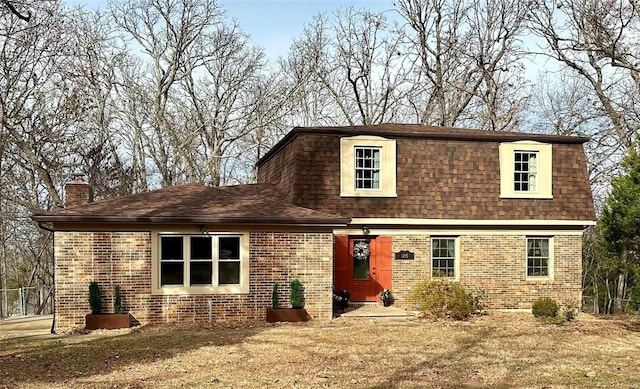 view of front of home with roof with shingles, a chimney, and brick siding