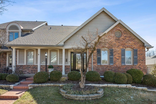 view of front of property with covered porch, brick siding, and roof with shingles