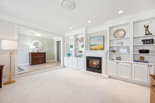 living room featuring built in shelves, baseboards, a lit fireplace, crown molding, and light colored carpet