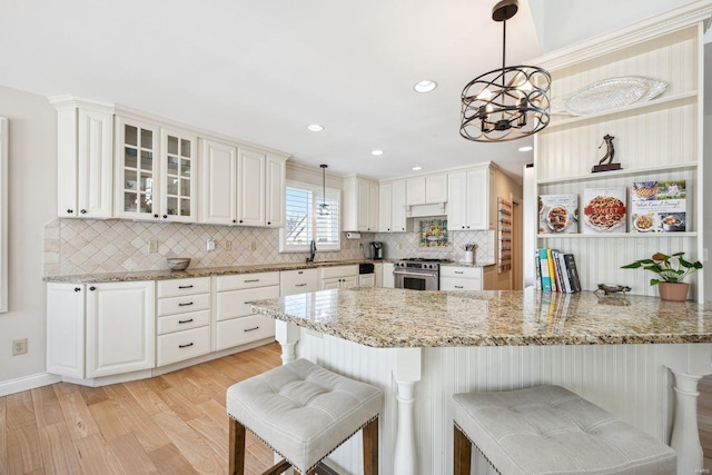 kitchen with a breakfast bar area, stainless steel stove, under cabinet range hood, light wood-type flooring, and backsplash