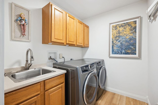 washroom featuring a sink, cabinet space, light wood-style floors, separate washer and dryer, and baseboards