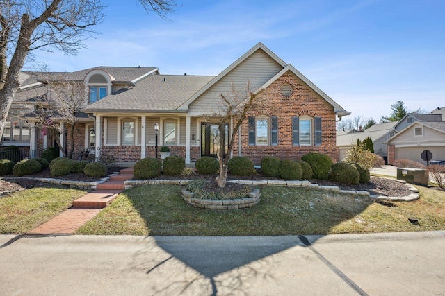 view of front facade featuring brick siding, a porch, a shingled roof, and a front yard