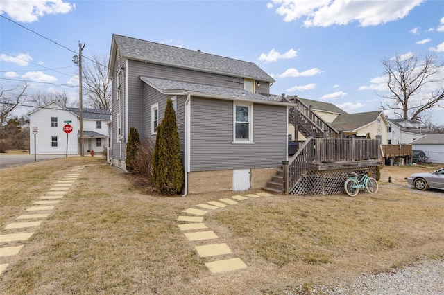 back of property with a shingled roof, a lawn, a deck, and stairs