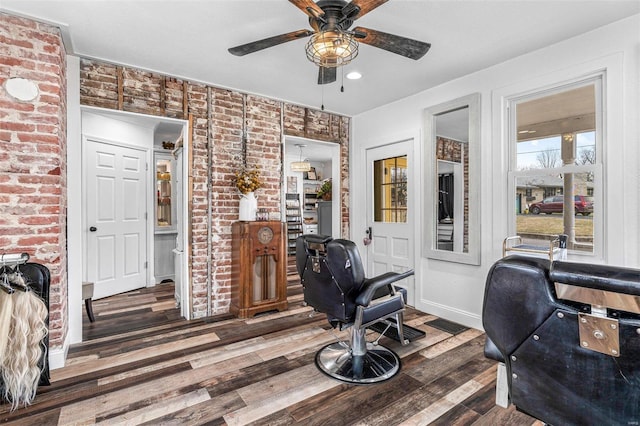 office space featuring a ceiling fan, brick wall, baseboards, and wood finished floors